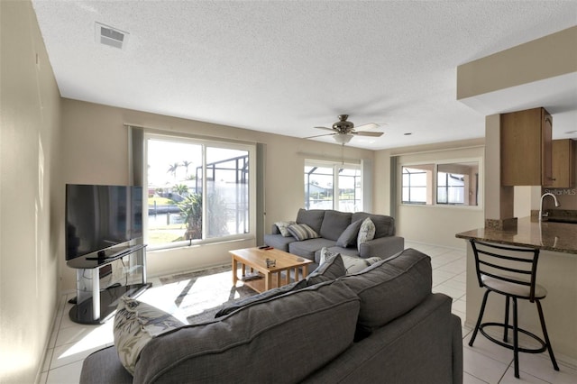 living area with a ceiling fan, visible vents, a textured ceiling, and light tile patterned floors