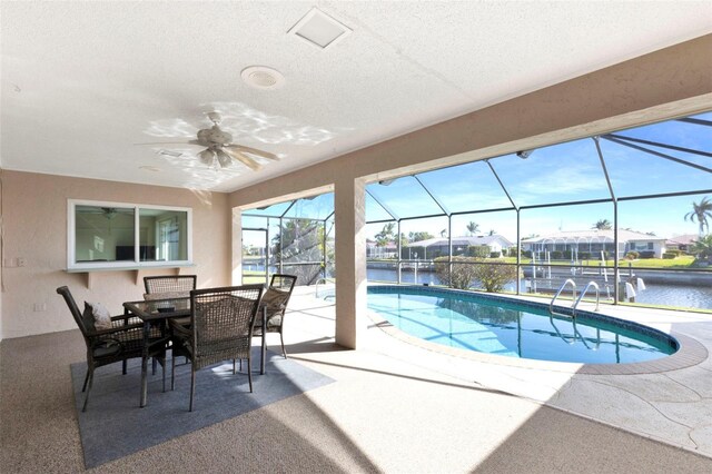 outdoor pool with outdoor dining area, a water view, a ceiling fan, glass enclosure, and a patio area