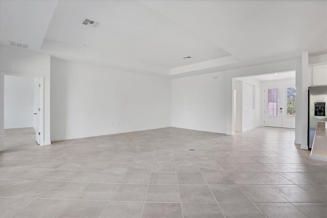 unfurnished living room with light tile patterned floors, visible vents, and a raised ceiling