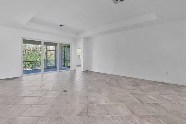 empty room with light tile patterned floors, visible vents, and a tray ceiling