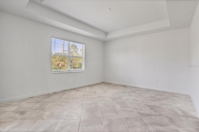 spare room with a raised ceiling, light tile patterned flooring, and baseboards