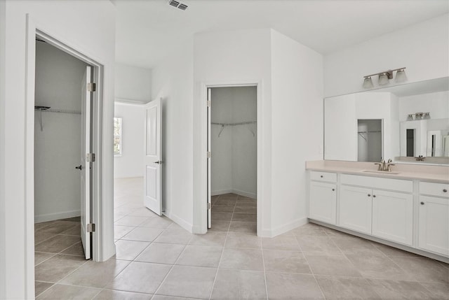 full bathroom featuring tile patterned flooring, a walk in closet, vanity, and baseboards