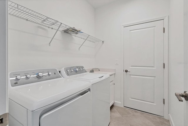 clothes washing area with cabinet space, light tile patterned floors, baseboards, washer and clothes dryer, and a sink