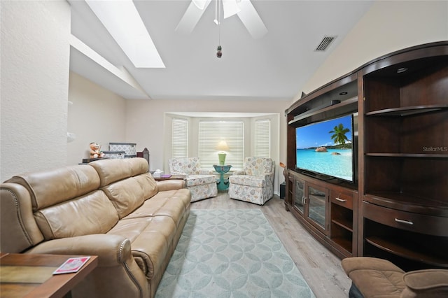 living area with a ceiling fan, vaulted ceiling with skylight, visible vents, and light wood finished floors