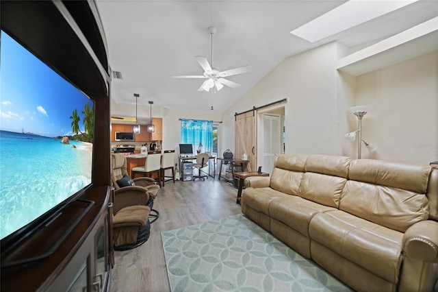 living area with a barn door, visible vents, a ceiling fan, lofted ceiling with skylight, and light wood-type flooring