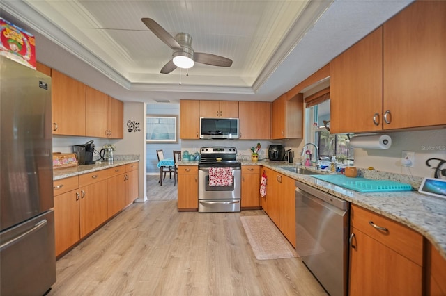 kitchen with a tray ceiling, crown molding, light wood finished floors, appliances with stainless steel finishes, and a sink