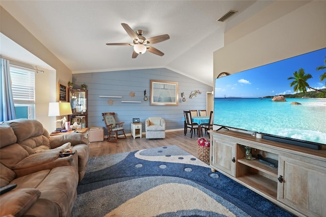 living room with ceiling fan, wood walls, wood finished floors, visible vents, and vaulted ceiling