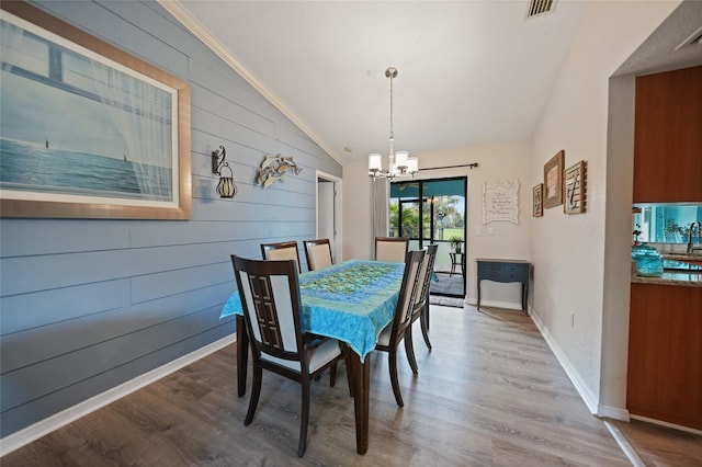 dining space with lofted ceiling, visible vents, an inviting chandelier, wood walls, and wood finished floors