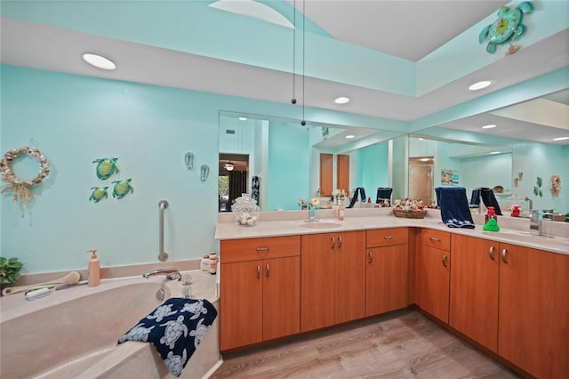 bathroom featuring a washtub, double vanity, a sink, and wood finished floors