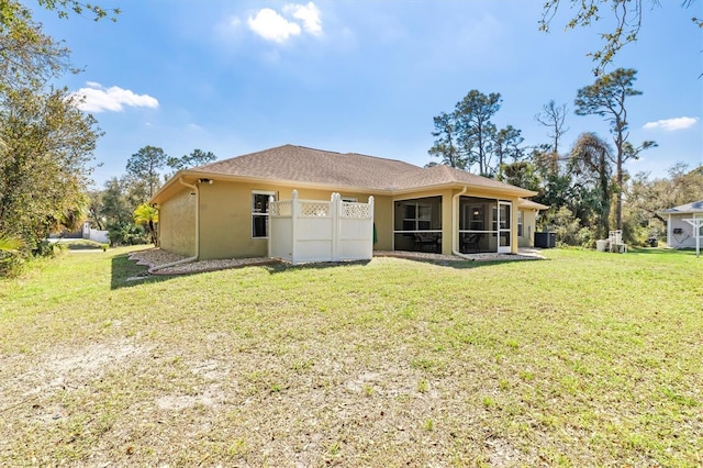 back of property featuring a sunroom, stucco siding, a yard, and central AC unit