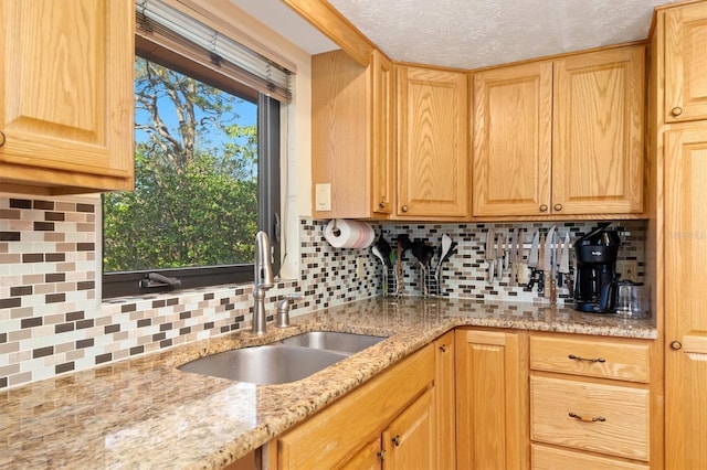 kitchen featuring light brown cabinets, tasteful backsplash, a sink, and light stone countertops