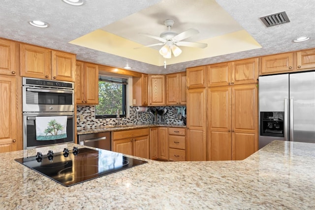 kitchen featuring tasteful backsplash, visible vents, appliances with stainless steel finishes, a tray ceiling, and a sink