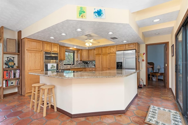 kitchen with stainless steel appliances, a tray ceiling, light stone countertops, and tasteful backsplash