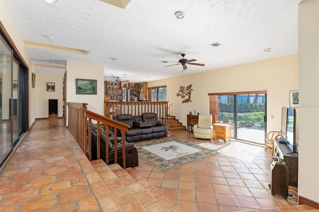 tiled living room with a textured ceiling, visible vents, a ceiling fan, and baseboards