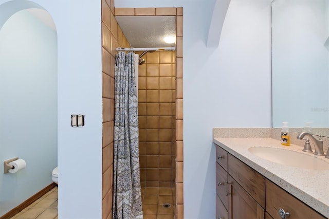 bathroom with toilet, vanity, tiled shower, baseboards, and tile patterned floors