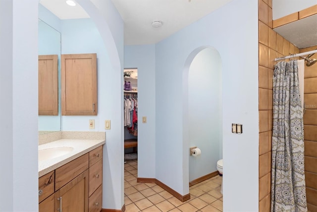 bathroom featuring tiled shower, toilet, tile patterned flooring, a spacious closet, and vanity