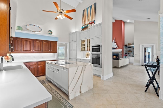 kitchen featuring a ceiling fan, a kitchen island, black electric cooktop, a fireplace, and a sink