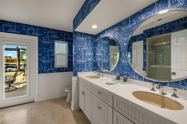 bathroom featuring wainscoting, a sink, toilet, and wallpapered walls