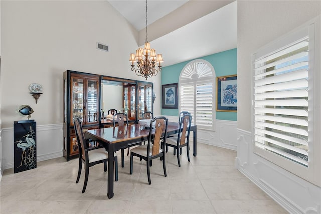 dining area with visible vents, lofted ceiling, a wainscoted wall, an inviting chandelier, and light tile patterned flooring