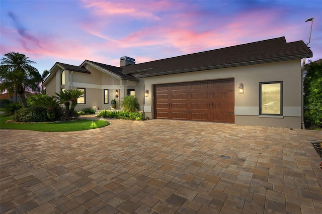 view of front of property featuring an attached garage, a chimney, decorative driveway, and stucco siding