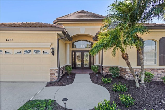 entrance to property featuring a garage, stucco siding, stone siding, and french doors