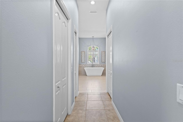 corridor featuring baseboards, visible vents, and light tile patterned flooring