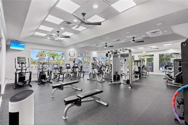 exercise room with baseboards, visible vents, ceiling fan, and a tray ceiling