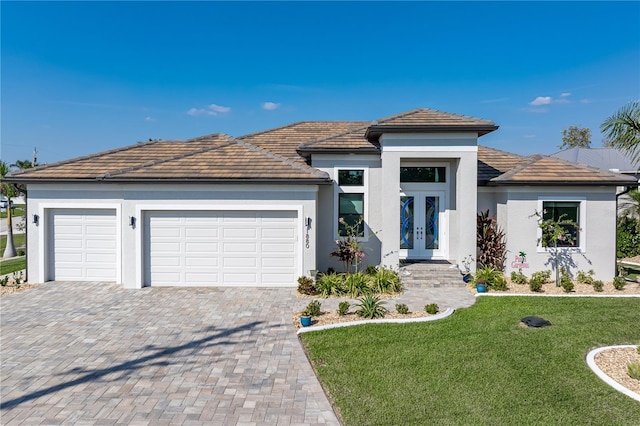 prairie-style house featuring a garage, decorative driveway, french doors, a front yard, and stucco siding