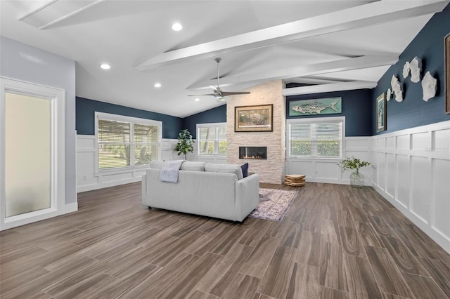 living area with lofted ceiling with beams, a stone fireplace, a wainscoted wall, and wood finished floors