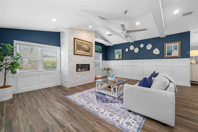 living room with vaulted ceiling with beams, a decorative wall, a fireplace, wood finished floors, and a ceiling fan