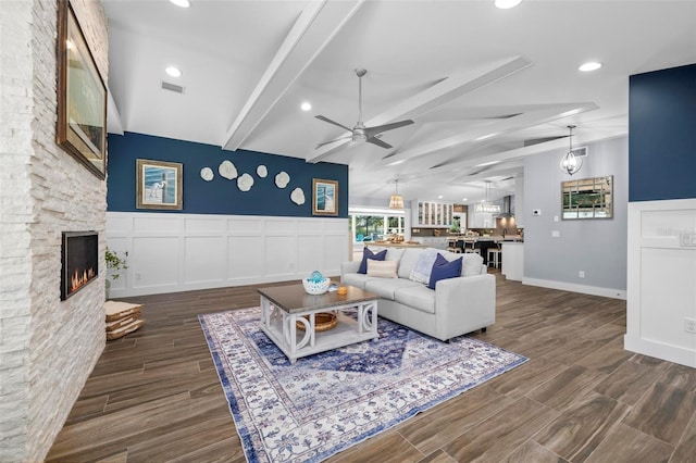 living area with beam ceiling, visible vents, dark wood-type flooring, ceiling fan, and a stone fireplace