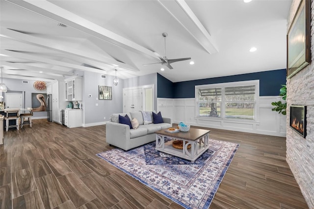 living room with lofted ceiling with beams, a wainscoted wall, a fireplace, and dark wood-type flooring