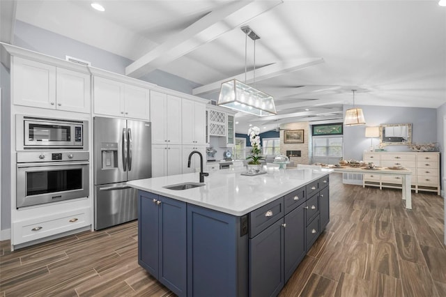 kitchen with wood finish floors, lofted ceiling with beams, appliances with stainless steel finishes, white cabinets, and a sink