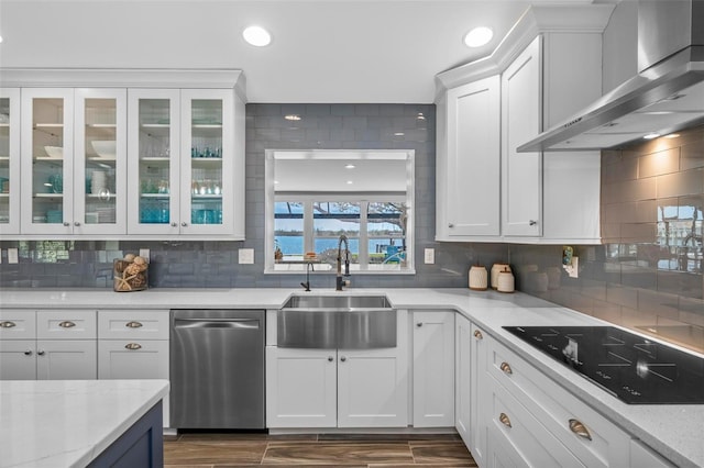 kitchen featuring dishwasher, black electric stovetop, wall chimney range hood, white cabinetry, and a sink