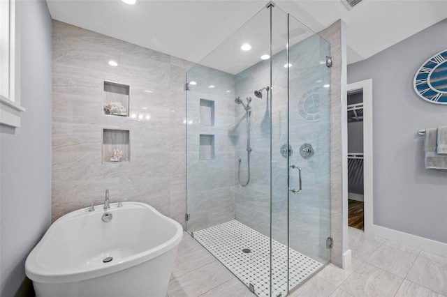 bathroom featuring a walk in closet, tile walls, a freestanding bath, a shower stall, and baseboards