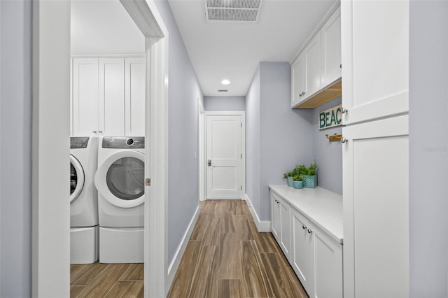 laundry room with wood finish floors, visible vents, baseboards, washer and dryer, and cabinet space