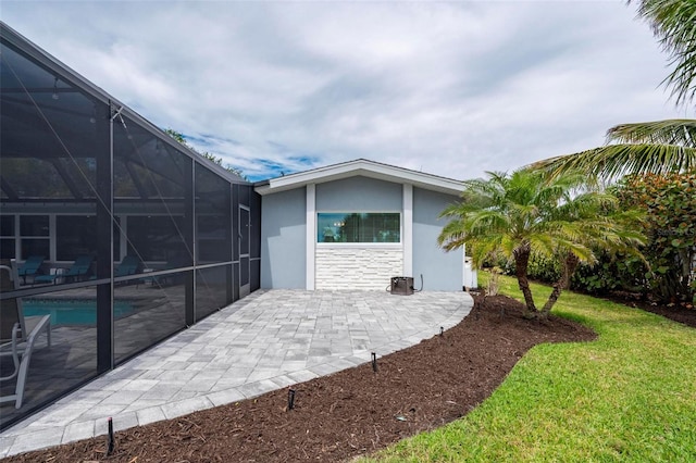 exterior space with a patio, stucco siding, glass enclosure, stone siding, and an outdoor pool