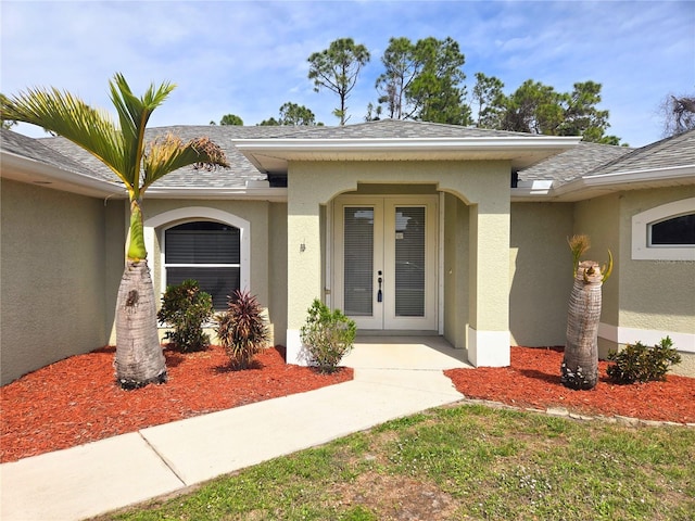 view of exterior entry with french doors, a shingled roof, and stucco siding