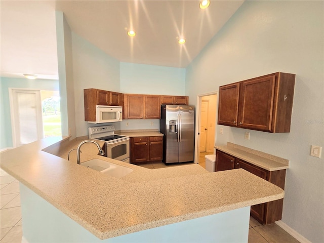 kitchen featuring light tile patterned floors, a high ceiling, a sink, white appliances, and a peninsula