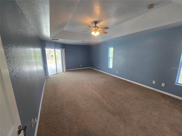 unfurnished room with ceiling fan, a textured ceiling, carpet floors, baseboards, and a raised ceiling