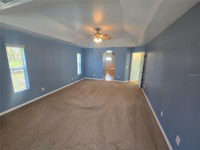 unfurnished room with arched walkways, carpet flooring, a raised ceiling, and baseboards