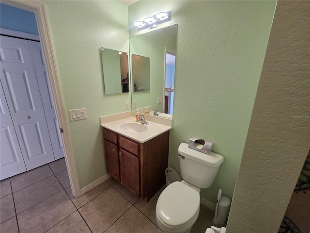 bathroom featuring a textured wall, toilet, vanity, baseboards, and tile patterned floors