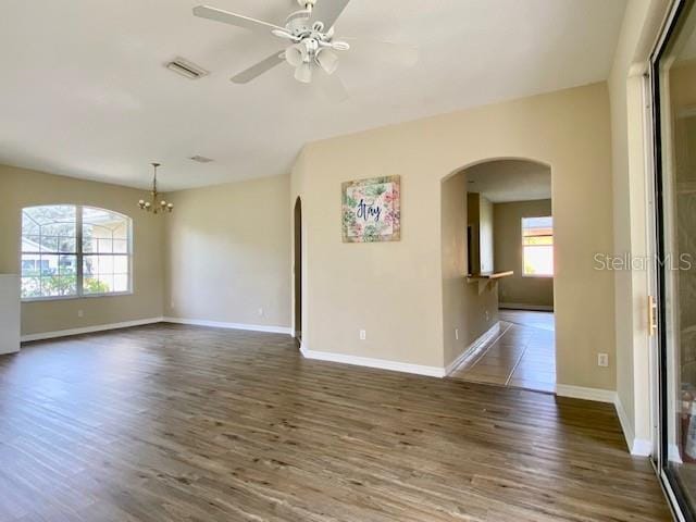 unfurnished room with baseboards, arched walkways, wood finished floors, and ceiling fan with notable chandelier