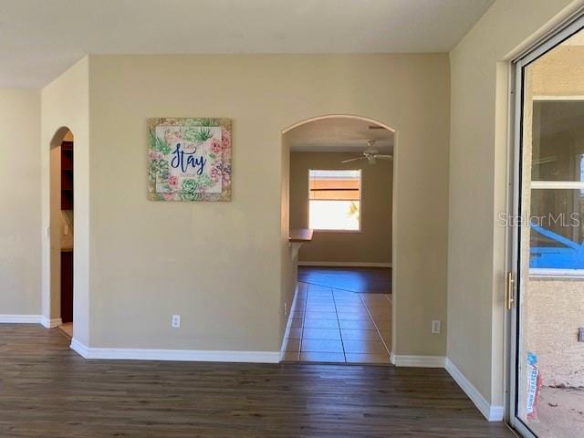 empty room with arched walkways, baseboards, a ceiling fan, and wood finished floors