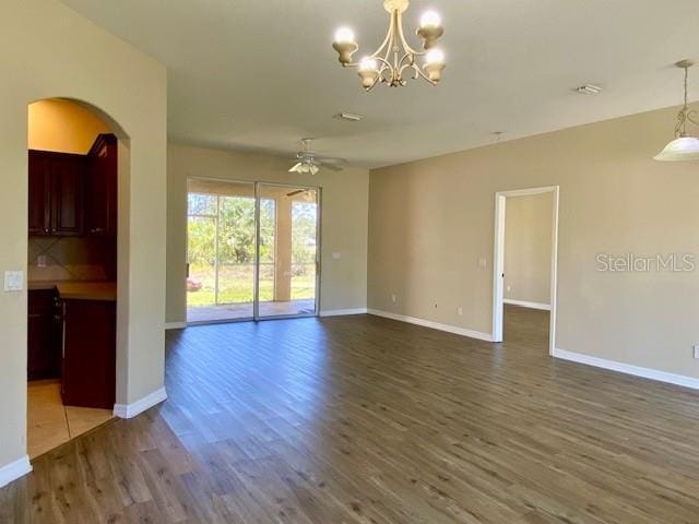 spare room featuring arched walkways, ceiling fan with notable chandelier, baseboards, and wood finished floors