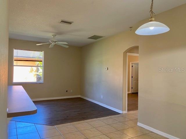 empty room with visible vents, baseboards, light tile patterned flooring, arched walkways, and a ceiling fan