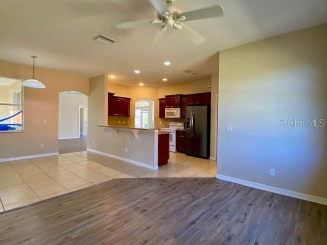 unfurnished living room featuring baseboards, light wood-style floors, arched walkways, and ceiling fan