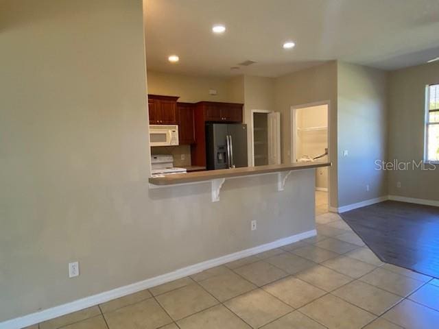 kitchen with white microwave, stainless steel fridge with ice dispenser, light countertops, a kitchen breakfast bar, and stove