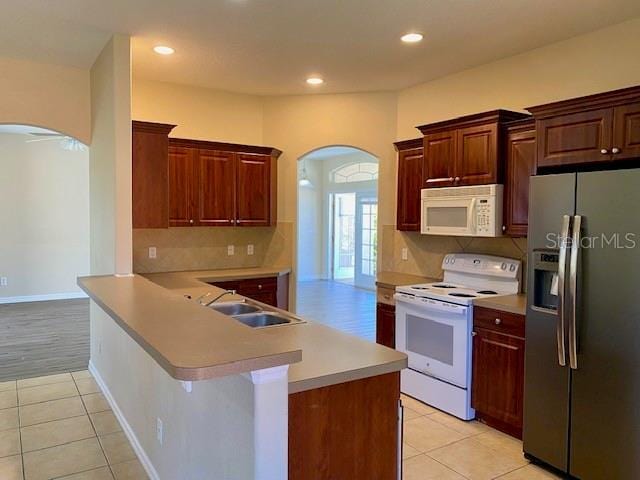 kitchen featuring white appliances, light tile patterned floors, arched walkways, and a sink