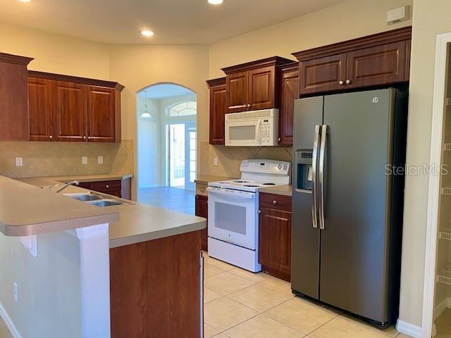 kitchen featuring tasteful backsplash, light countertops, arched walkways, white appliances, and a sink